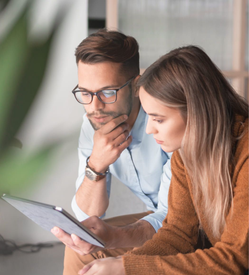 Junger Mann mit Brille und Junge Frau schauen gemeinsam auf ein Tablet