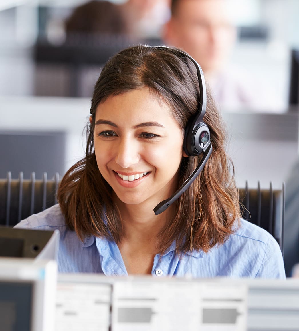 Lächelnde junge Frau mit Headset sitzt vor einem PC und telefoniert mit einem Kunden